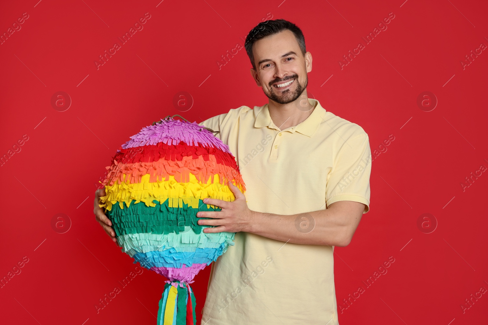 Photo of Happy man with colorful pinata on red background