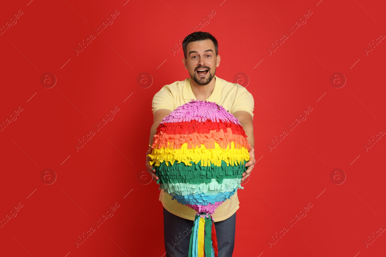 Photo of Emotional man with colorful pinata on red background