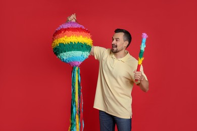 Photo of Happy man with colorful pinata and stick on red background