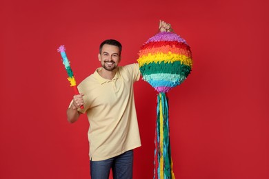 Photo of Happy man with colorful pinata and stick on red background