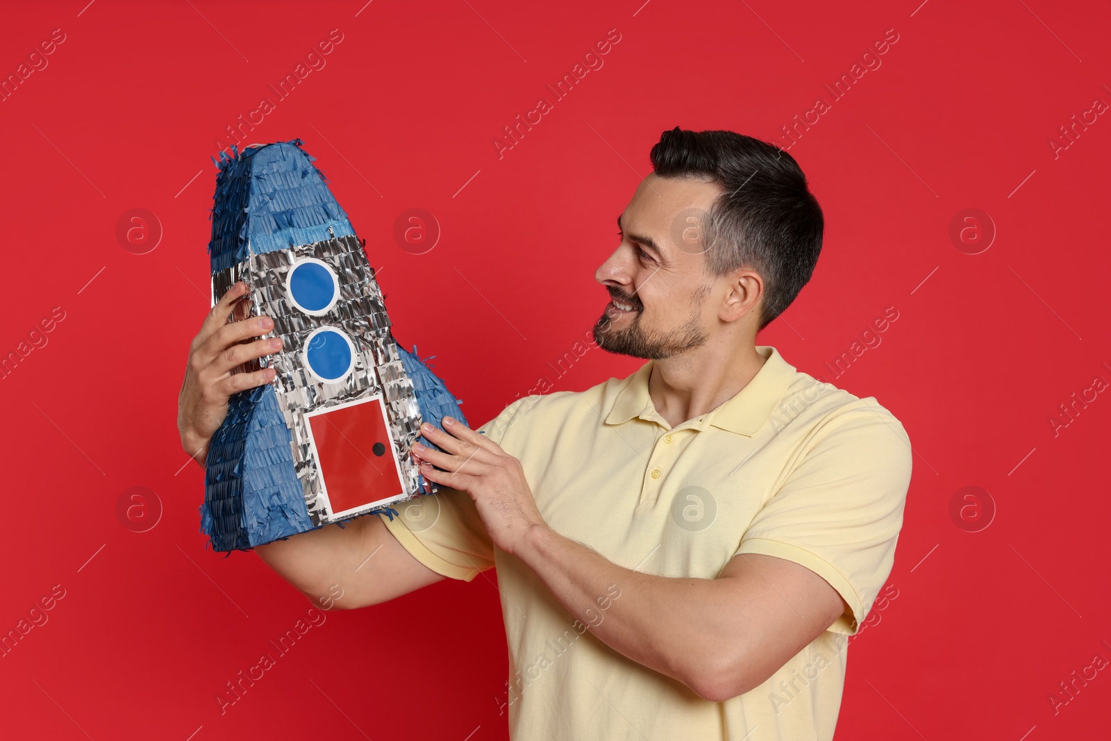 Photo of Happy man with rocket shaped pinata on red background