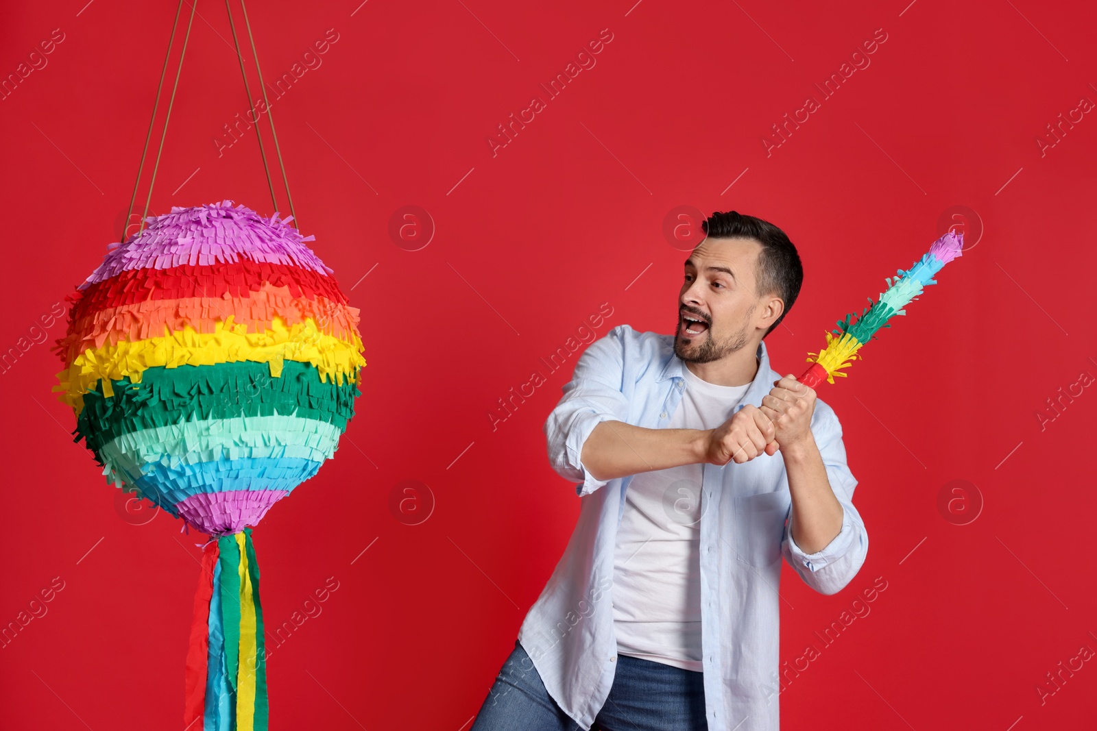 Photo of Happy man hitting colorful pinata with stick on red background