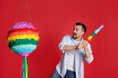 Photo of Happy man hitting colorful pinata with stick on red background