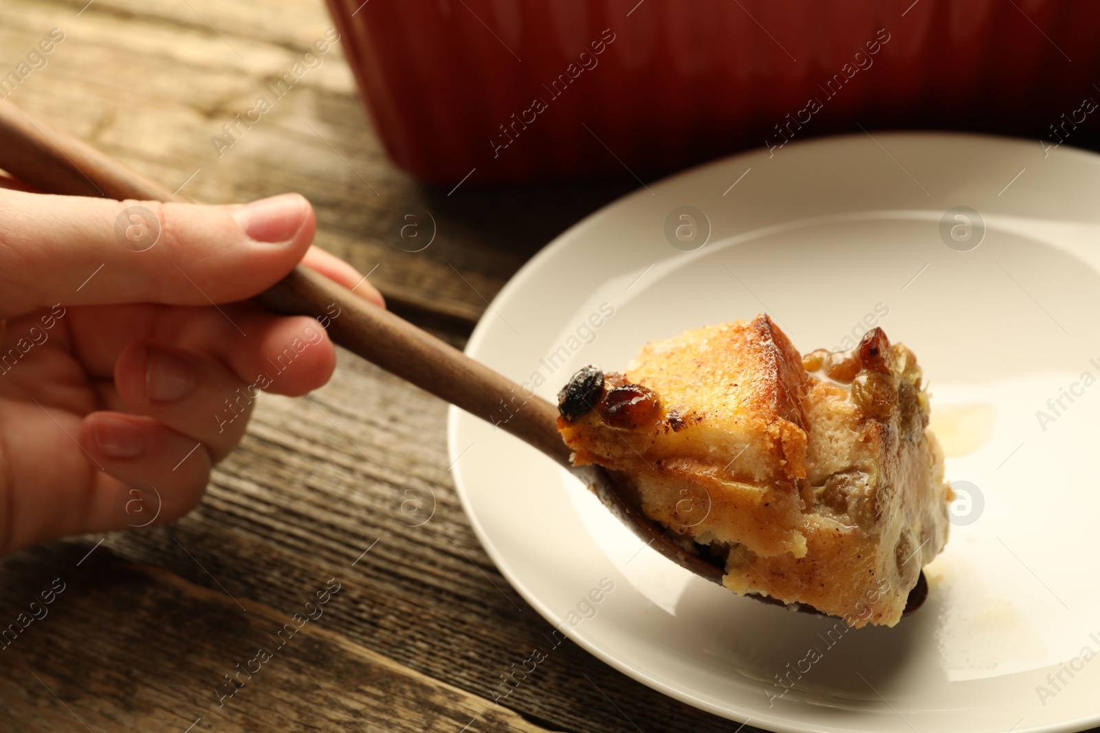 Photo of Woman eating tasty bread pudding at wooden table, closeup