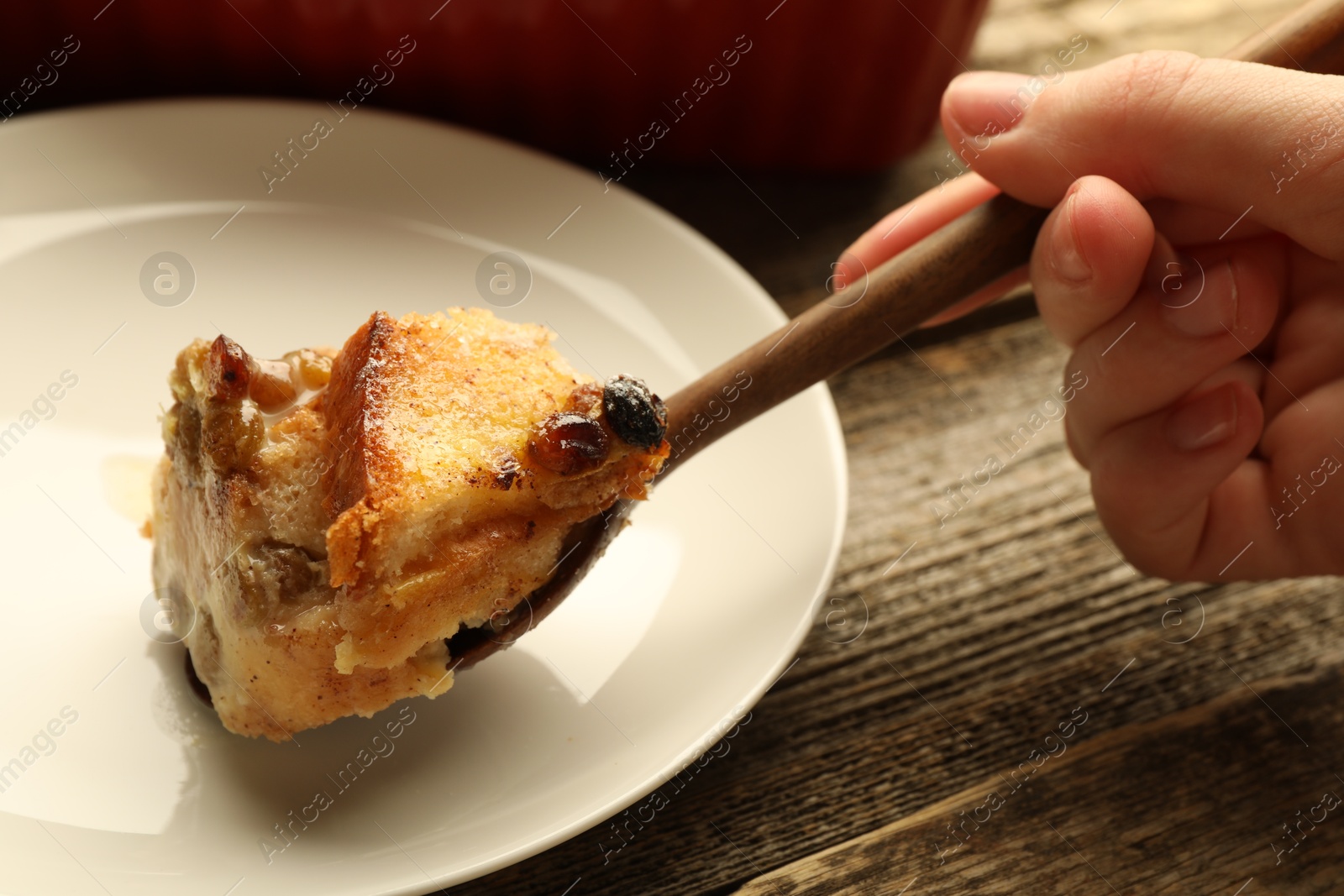 Photo of Woman eating tasty bread pudding at wooden table, closeup