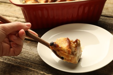 Photo of Woman eating tasty bread pudding at wooden table, closeup