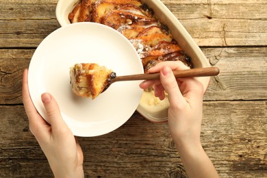 Photo of Woman eating tasty bread pudding at wooden table, top view