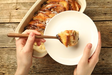 Photo of Woman eating tasty bread pudding at wooden table, top view