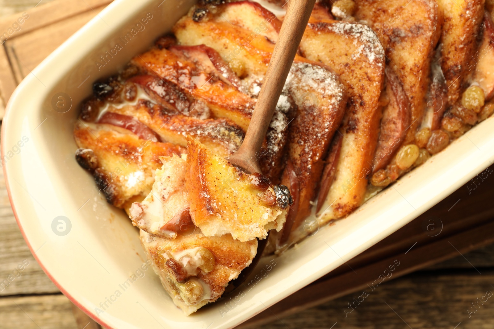 Photo of Taking tasty bread pudding from baking dish at wooden table, top view