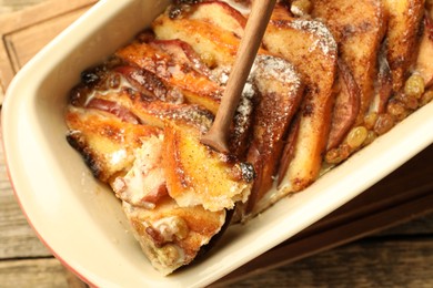 Taking tasty bread pudding from baking dish at wooden table, top view