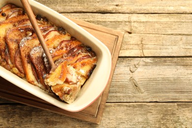 Photo of Taking tasty bread pudding from baking dish at wooden table, top view. Space for text