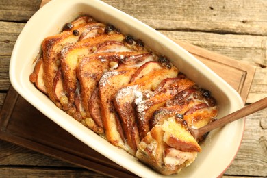 Photo of Taking tasty bread pudding from baking dish at wooden table, top view