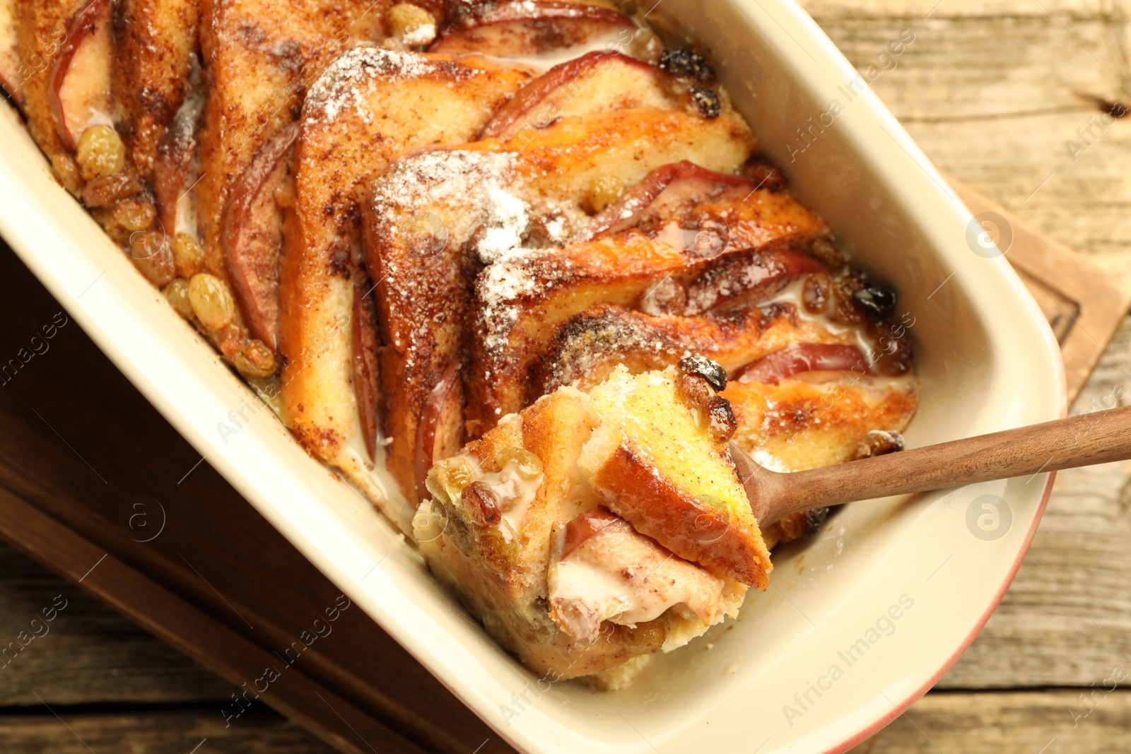 Photo of Taking tasty bread pudding from baking dish at wooden table, top view