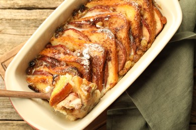 Photo of Taking tasty bread pudding from baking dish at wooden table, top view