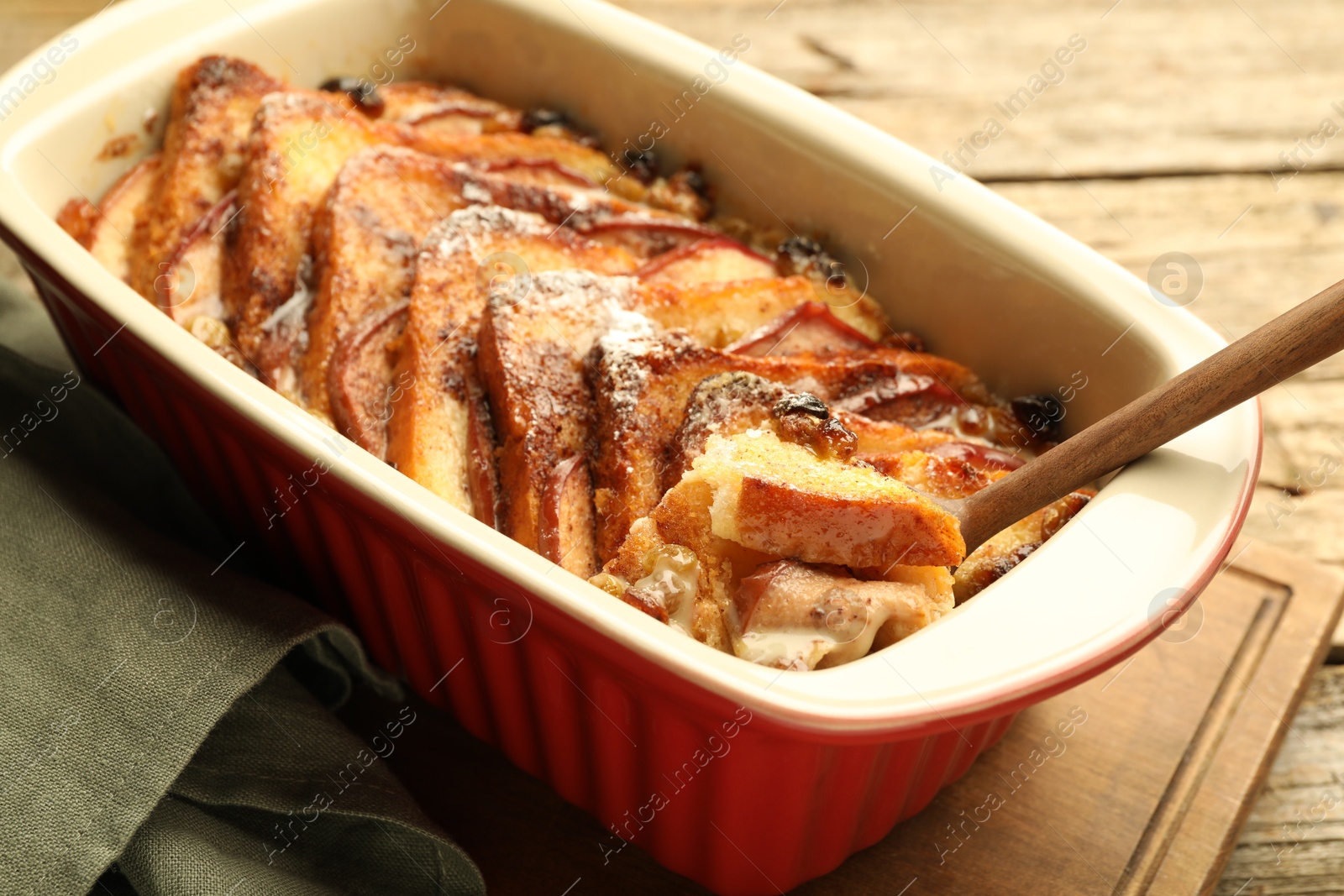 Photo of Taking tasty bread pudding from baking dish at wooden table, closeup