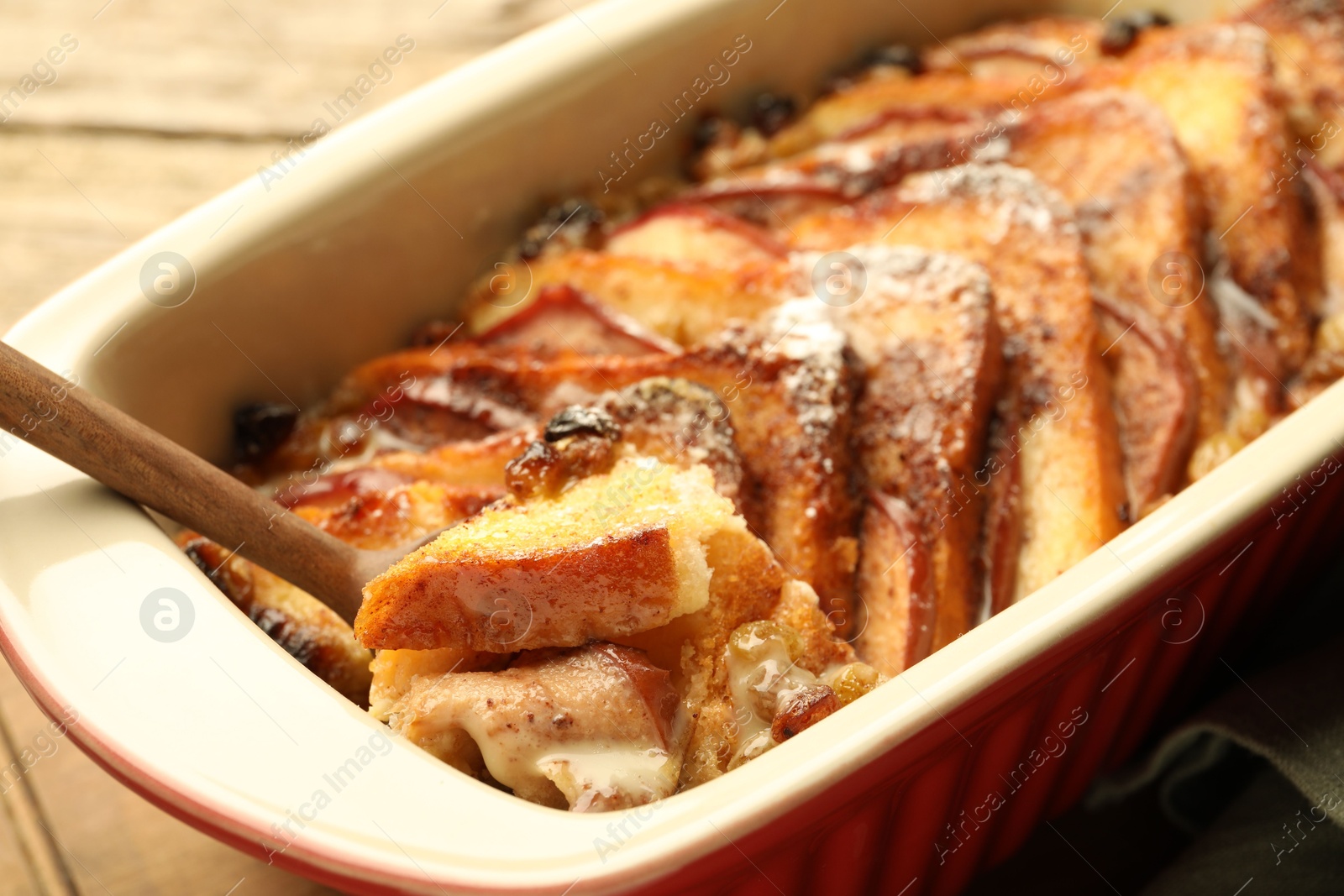 Photo of Taking tasty bread pudding from baking dish at wooden table, closeup