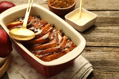 Photo of Freshly baked bread pudding in baking dish and spoon on wooden table, closeup