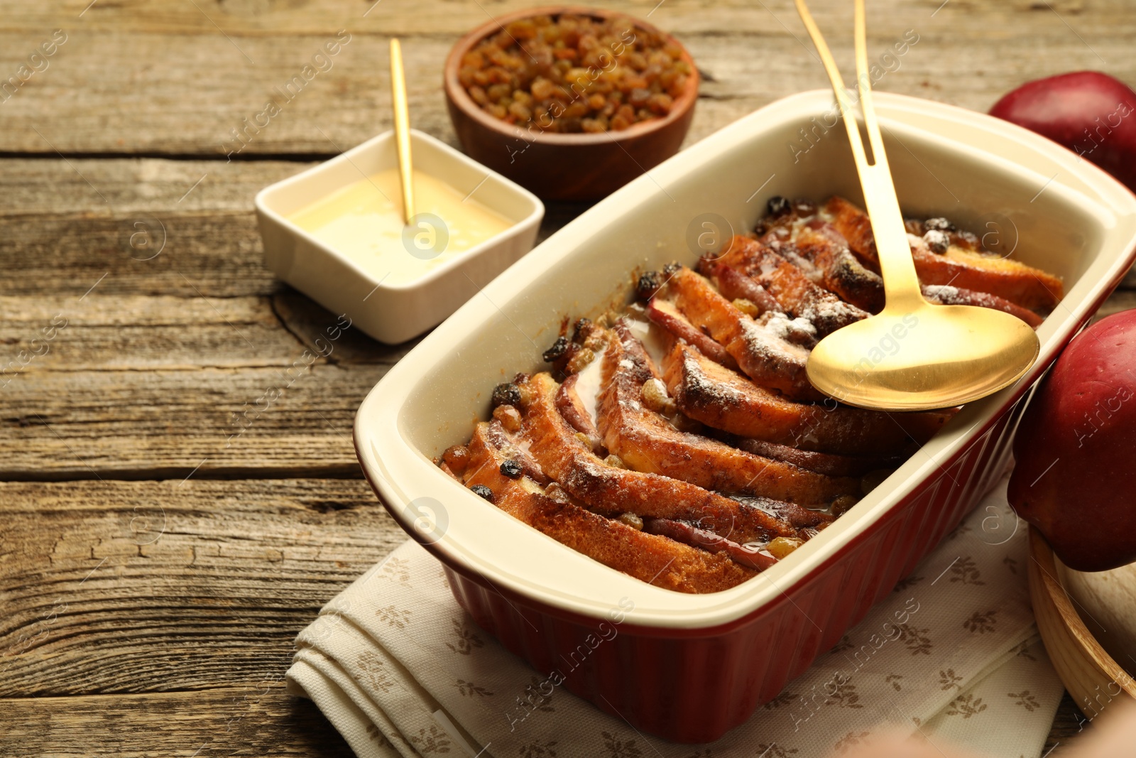 Photo of Freshly baked bread pudding in baking dish and spoon on wooden table, closeup