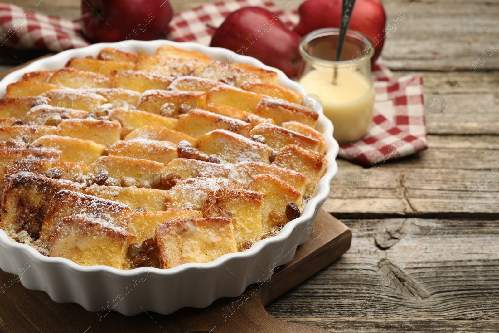 Photo of Delicious bread pudding with raisins, powdered sugar, condensed milk and apples on wooden table, closeup