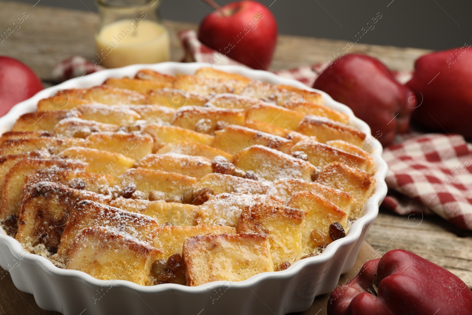 Photo of Delicious bread pudding with raisins, powdered sugar and apples on wooden table, closeup