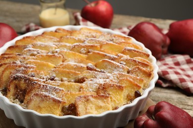 Photo of Delicious bread pudding with raisins, powdered sugar and apples on wooden table, closeup