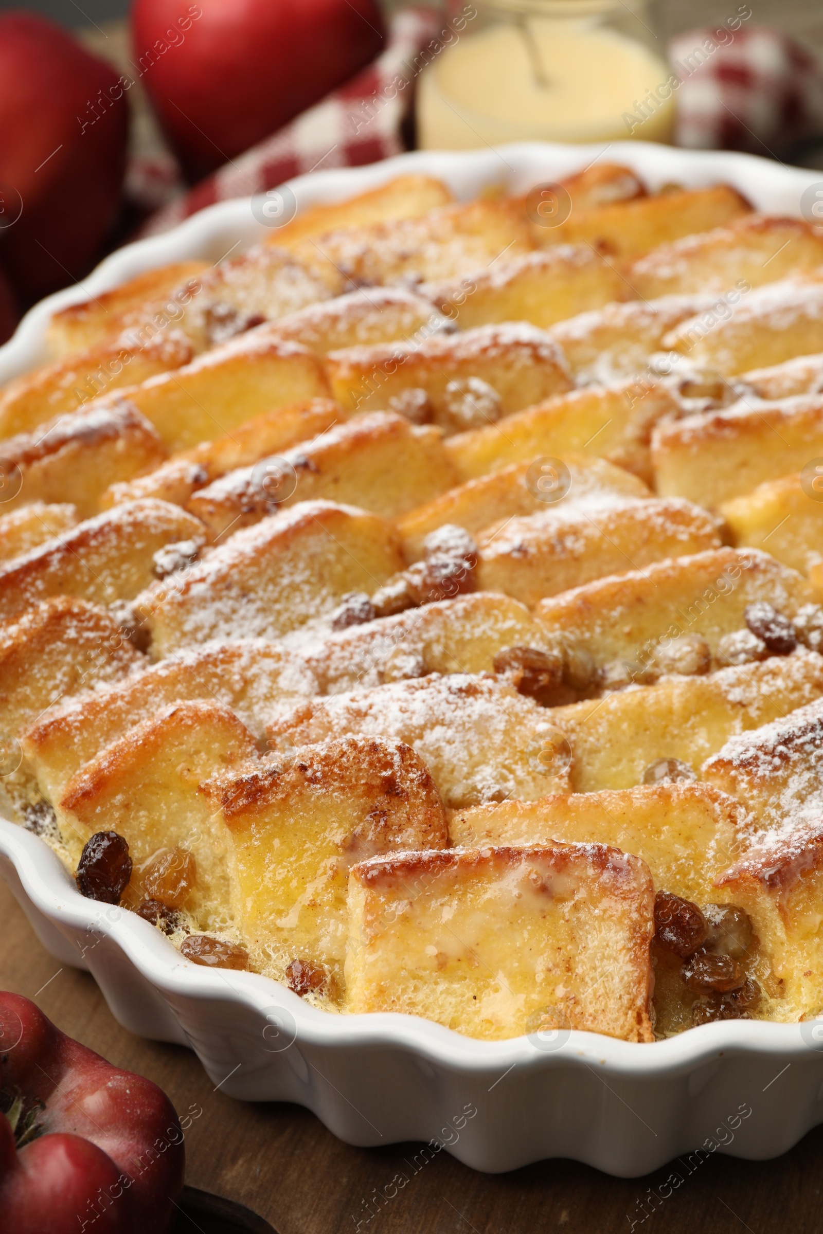 Photo of Delicious bread pudding with raisins, powdered sugar and apples on wooden table, closeup