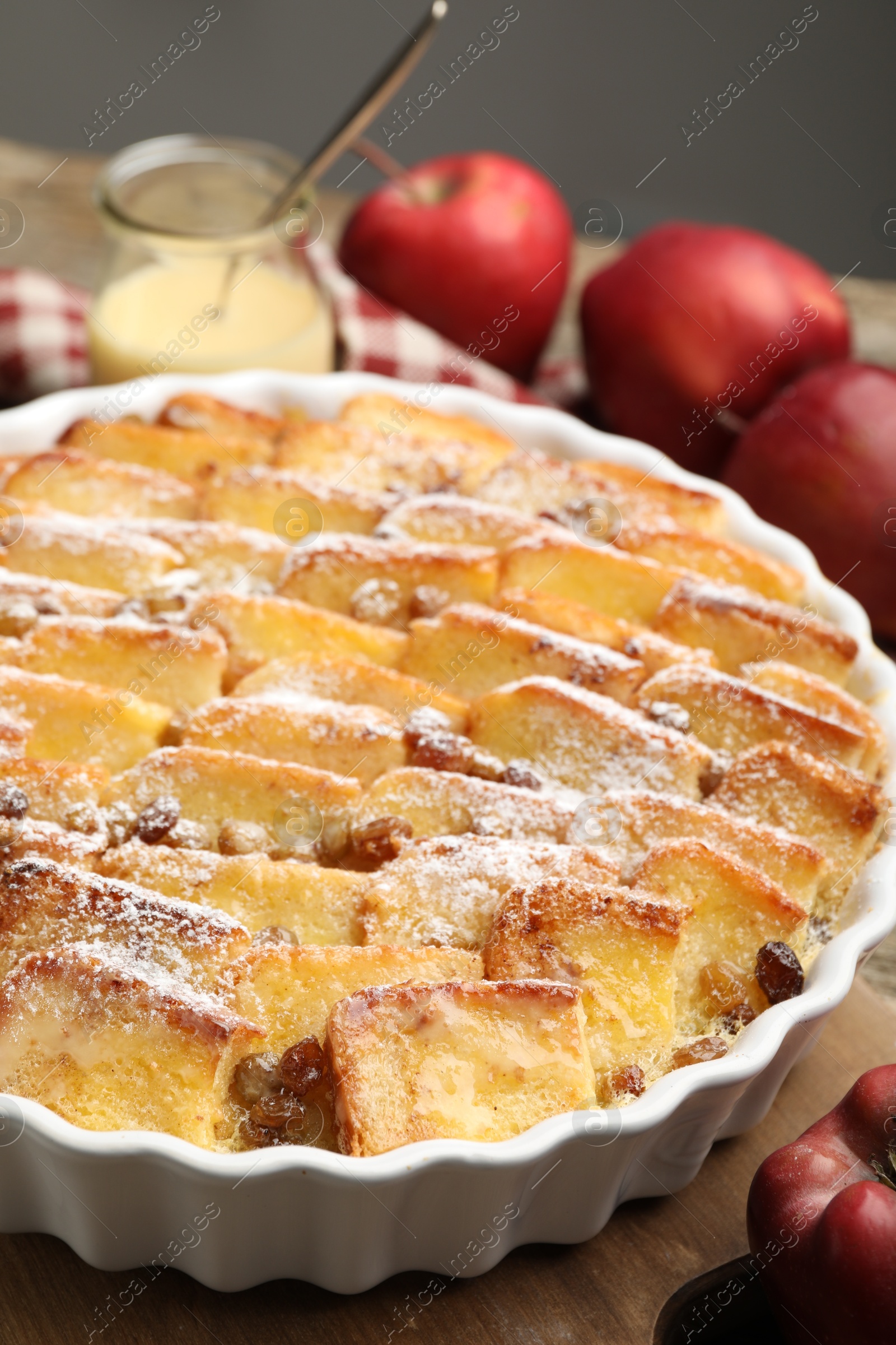 Photo of Delicious bread pudding with raisins, powdered sugar, condensed milk and apples on wooden table, closeup