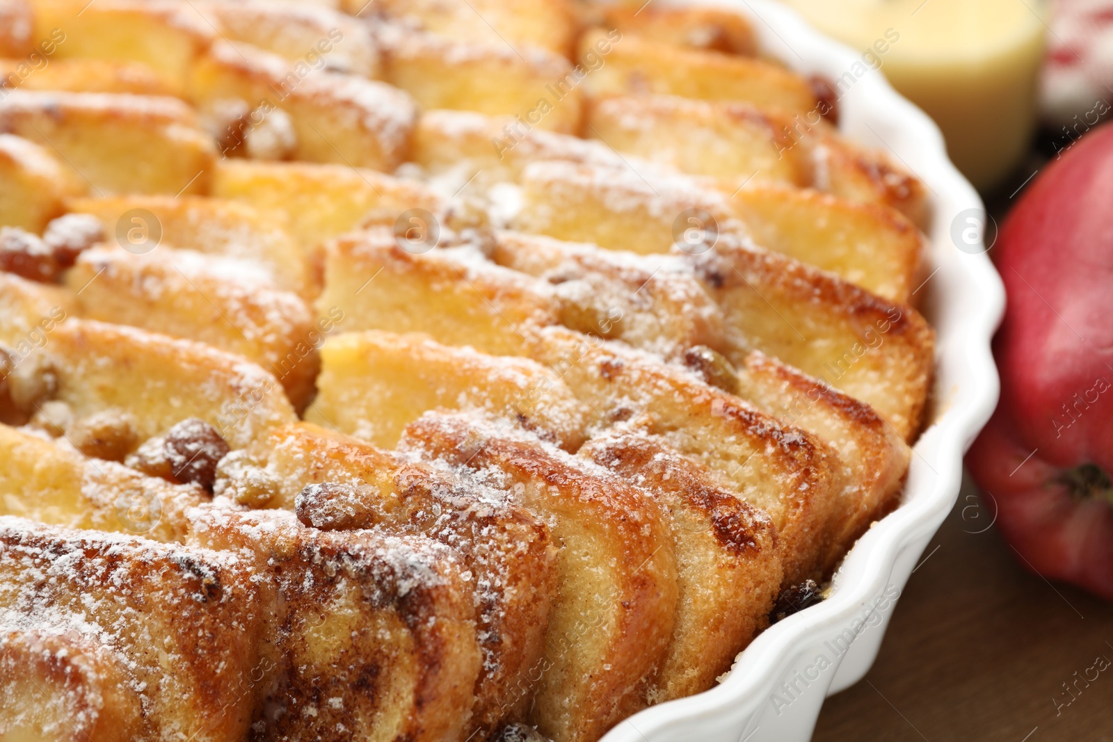 Photo of Delicious bread pudding with raisins, powdered sugar and apple on wooden table, closeup