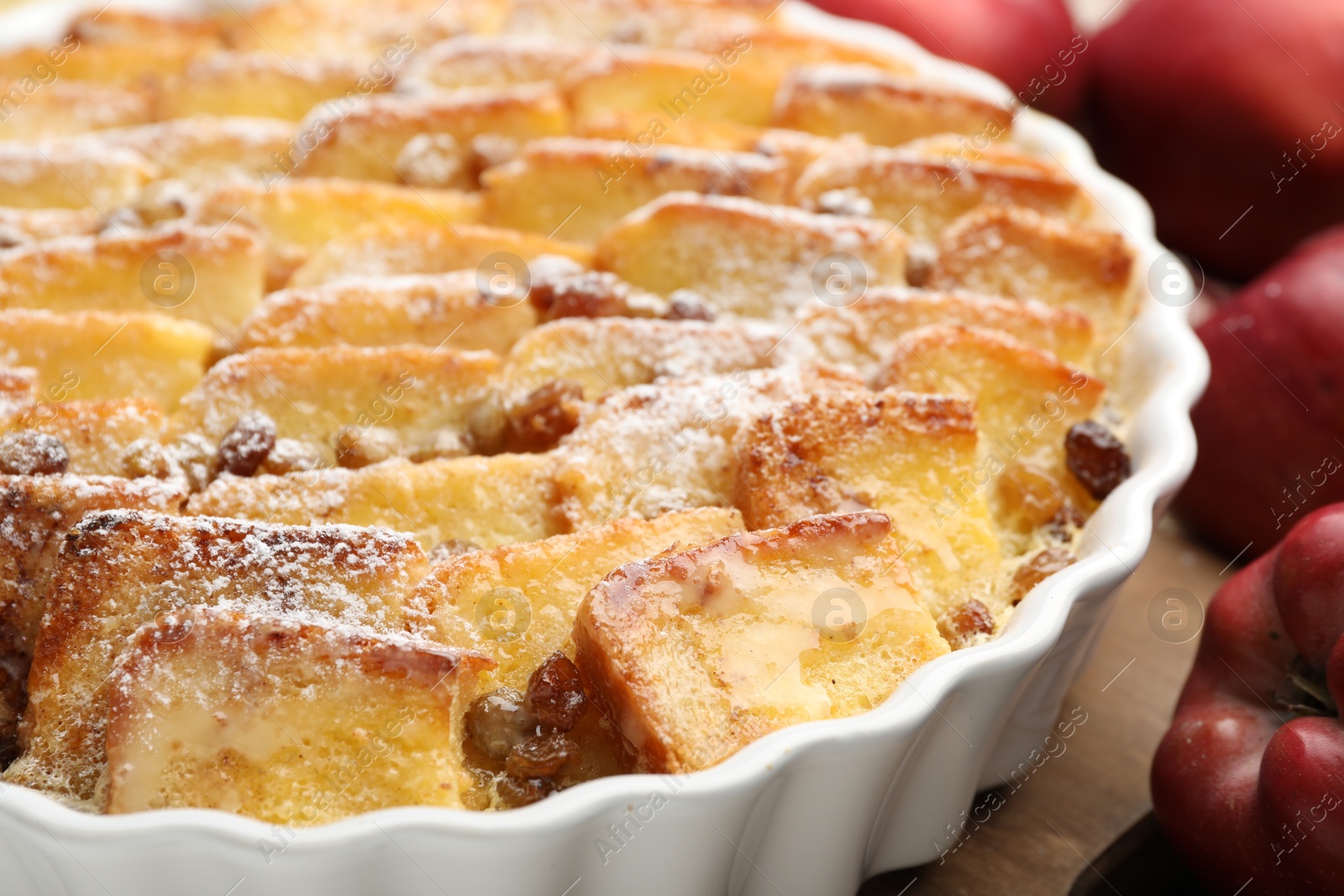 Photo of Delicious bread pudding with raisins, powdered sugar and apples on wooden table, closeup