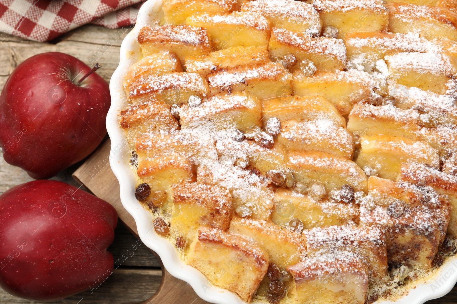 Photo of Delicious bread pudding with raisins, powdered sugar and apples on wooden table, top view