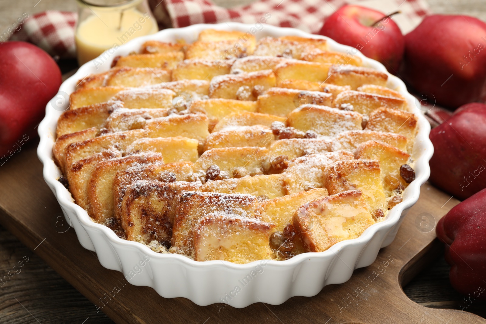 Photo of Delicious bread pudding with raisins, powdered sugar and apples on wooden table, closeup