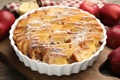 Photo of Delicious bread pudding with raisins, powdered sugar and apples on wooden table, closeup