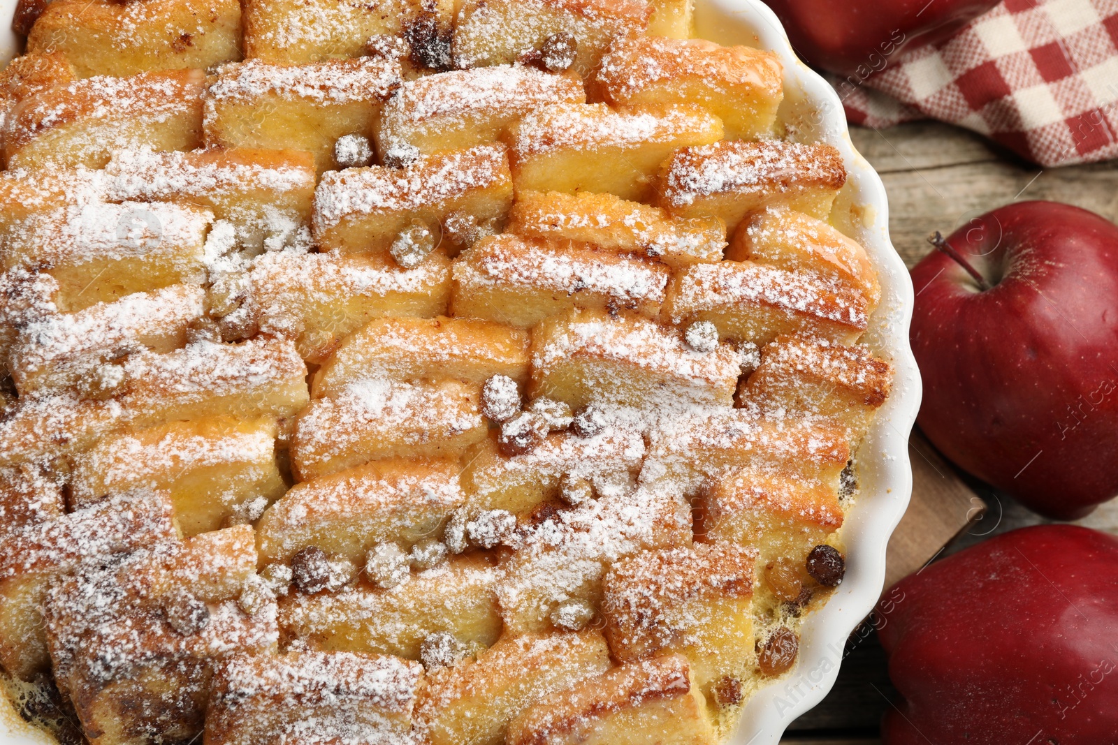 Photo of Delicious bread pudding with raisins, powdered sugar and apples on wooden table, top view