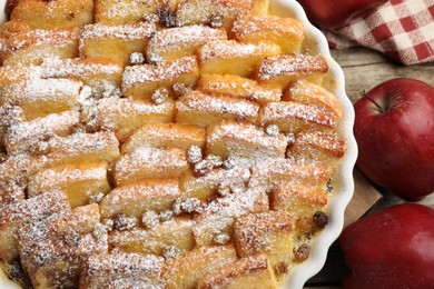 Photo of Delicious bread pudding with raisins, powdered sugar and apples on wooden table, top view