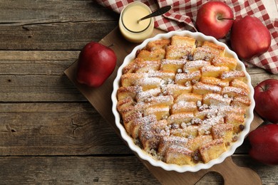 Photo of Delicious bread pudding with raisins, powdered sugar, condensed milk and apples on wooden table, flat lay