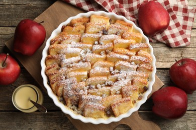 Photo of Delicious bread pudding with raisins, powdered sugar, condensed milk and apples on wooden table, flat lay