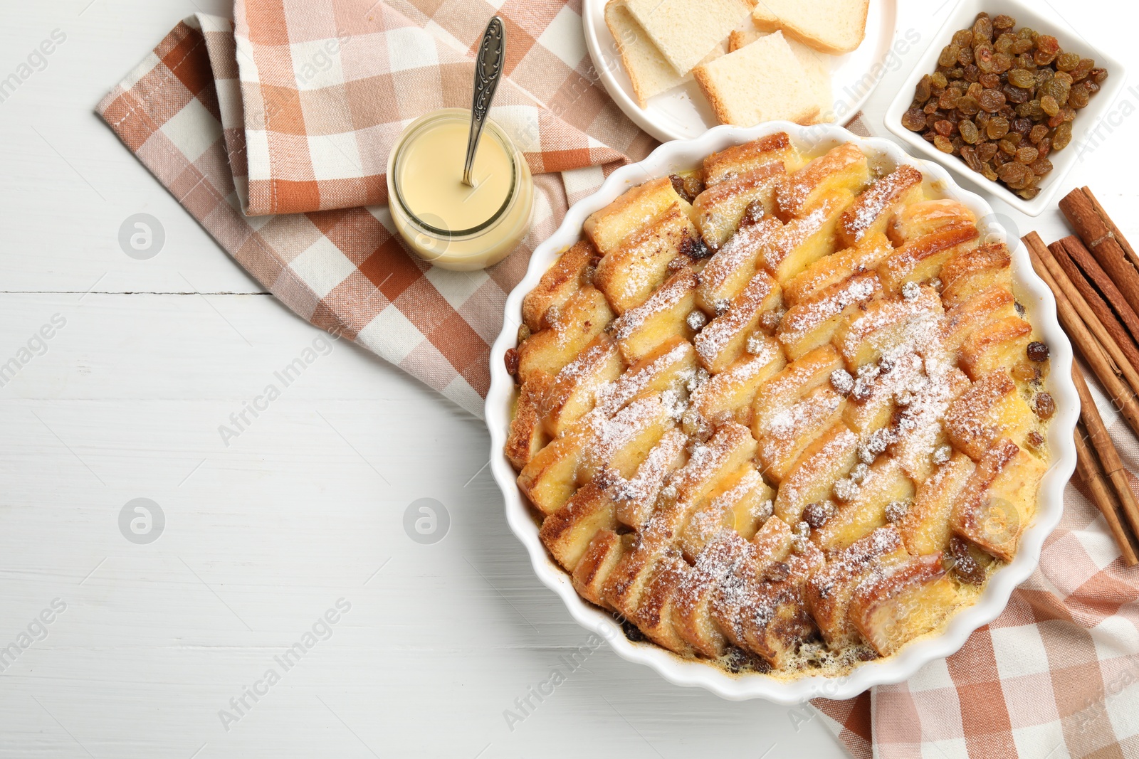 Photo of Delicious bread pudding with raisins, powdered sugar, condensed milk on white wooden table, flat lay. Space for text