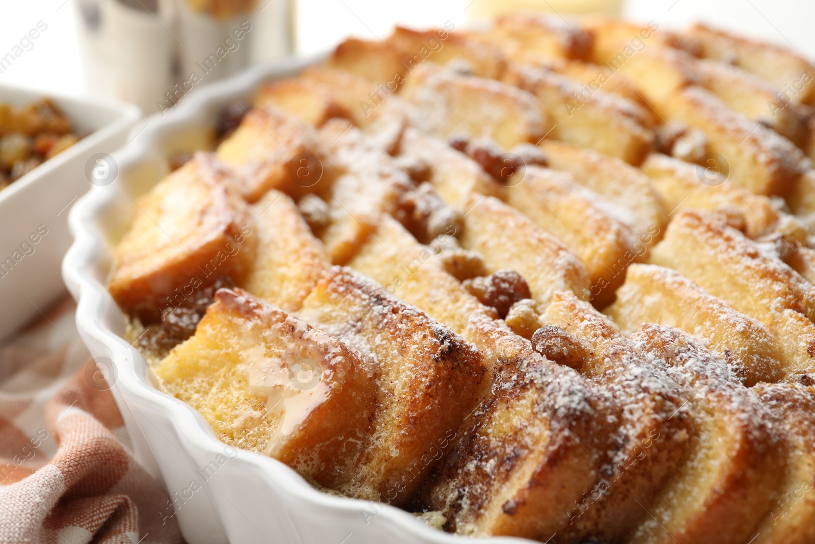 Photo of Delicious bread pudding with raisins and powdered sugar in dish, closeup