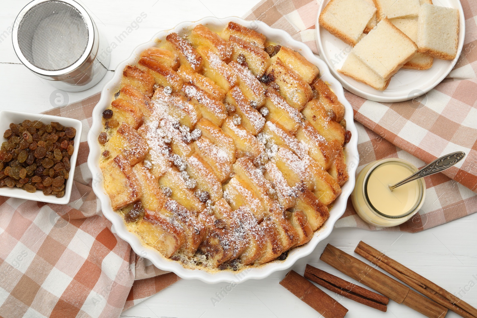 Photo of Delicious bread pudding with raisins, powdered sugar, condensed milk on white wooden table, flat lay