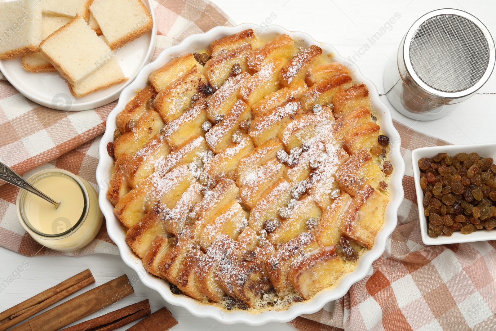 Photo of Delicious bread pudding with raisins, powdered sugar, condensed milk on white wooden table, flat lay