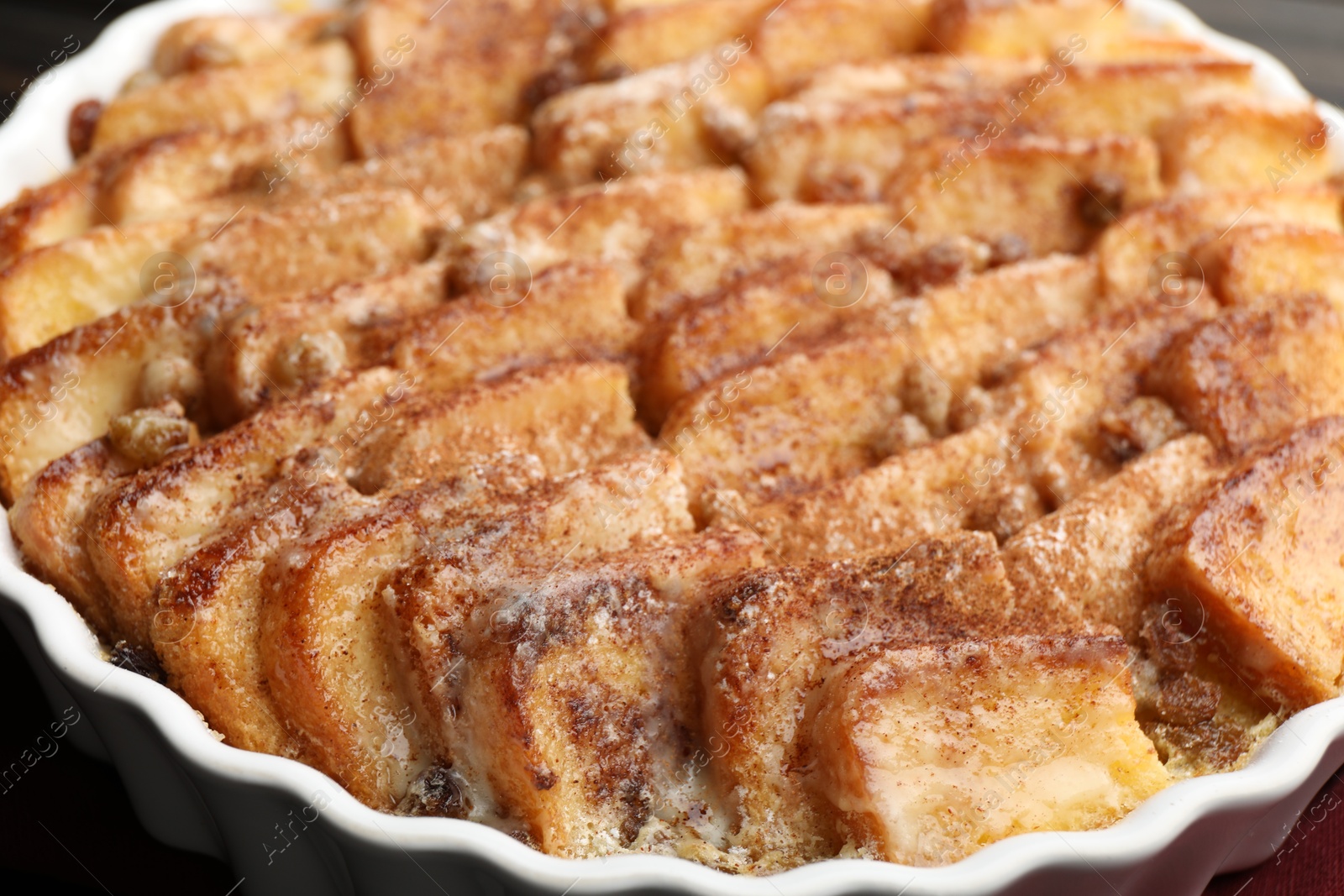 Photo of Delicious bread pudding with raisins and cinnamon in dish, closeup