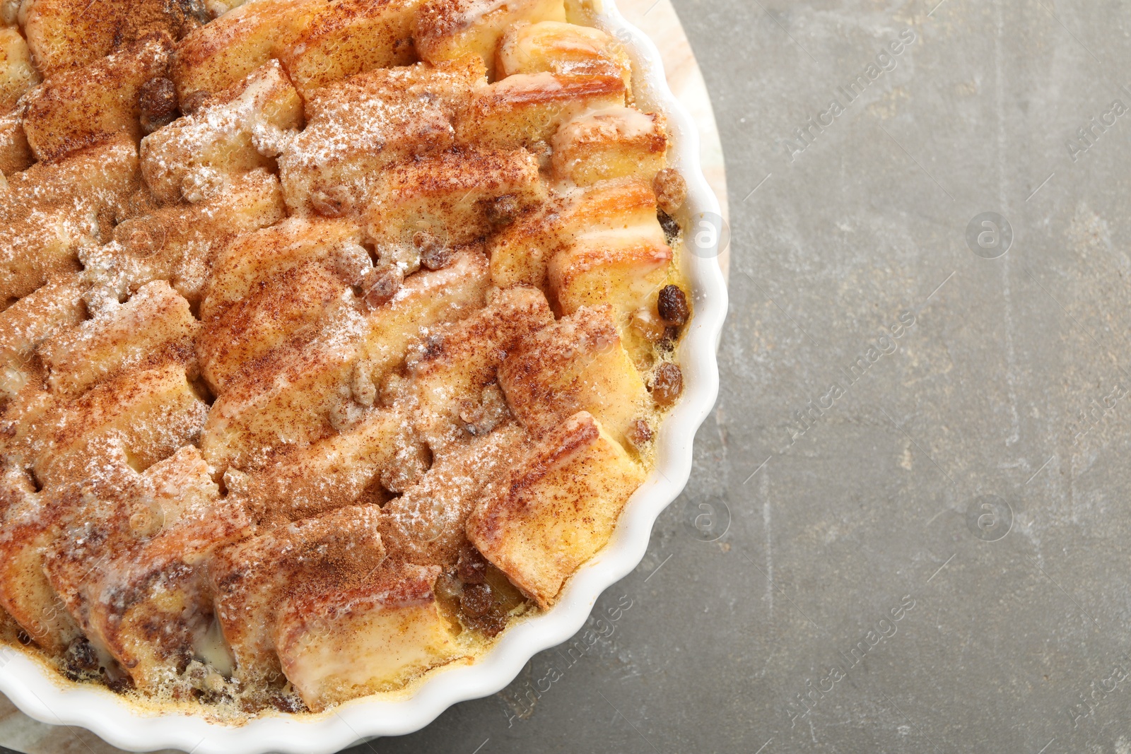 Photo of Delicious bread pudding with raisins and cinnamon on grey table, top view. Space for text