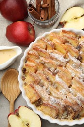 Photo of Delicious bread pudding with raisins, powdered sugar and apples on grey table, flat lay