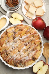 Photo of Delicious bread pudding with raisins, powdered sugar and apples on grey table, flat lay