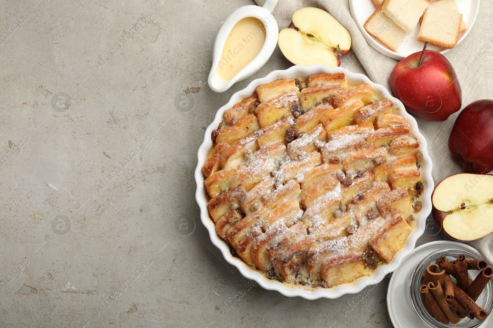 Photo of Delicious bread pudding with raisins, powdered sugar and apples on grey table, flat lay. Space for text