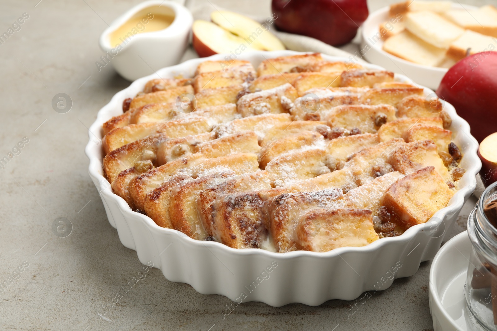 Photo of Delicious bread pudding with raisins, powdered sugar and apples on grey table, closeup