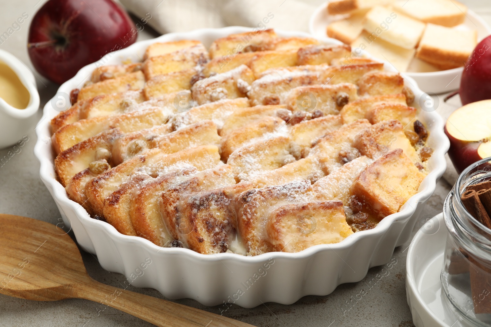 Photo of Delicious bread pudding with raisins, powdered sugar and apples on grey table, closeup