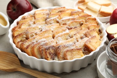 Photo of Delicious bread pudding with raisins, powdered sugar and apples on grey table, closeup