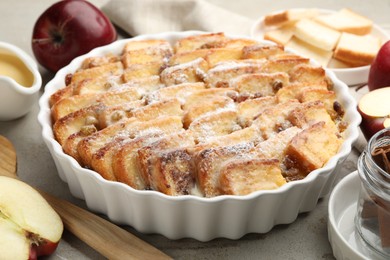 Photo of Delicious bread pudding with raisins, powdered sugar and apples on grey table, closeup