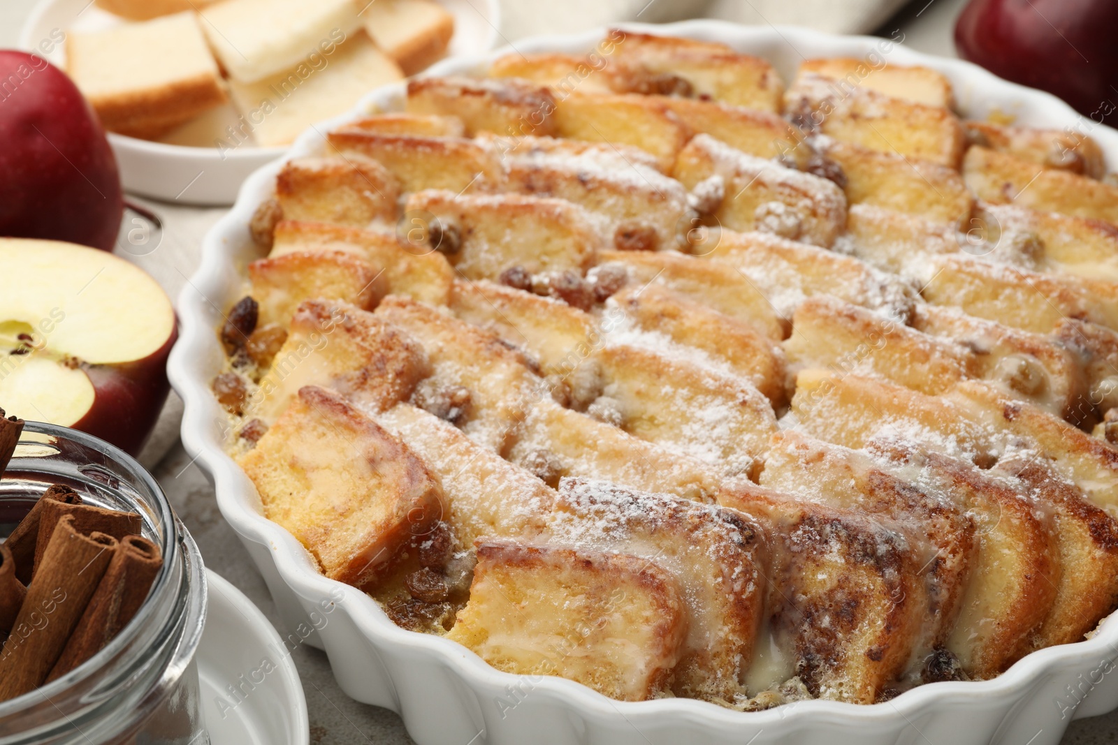 Photo of Delicious bread pudding with raisins, powdered sugar, cinnamon and apples on table, closeup